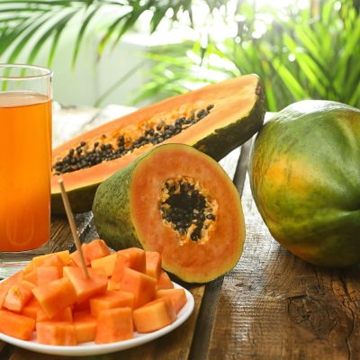 Fresh papayas and juice on wooden table against blurred background
